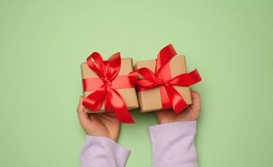 Woman's hand holding a gift box wrapped in a red silk ribbon on a green background