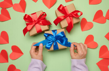 Woman's hand holding a gift box wrapped in a red silk ribbon on a green background