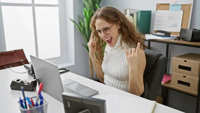 Crazy expression on beautiful young woman at office, working with rock star energy, showcasing heavy metal hand symbol
