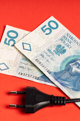 money Polish zloty banknotes and black electric cable with plug lying on red background (selective focus)