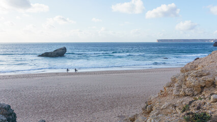 Two surfer at Praia do Tonel beach walking with boards into the sea, Sagres, Algarve, Portugal