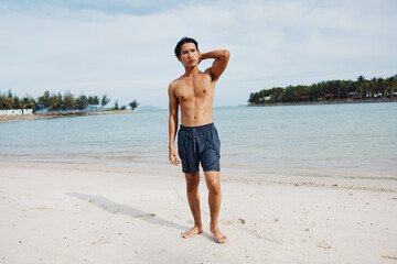 Smiling Asian Man Enjoying Beach Vacation: Muscular Torso and Happy Smile against Tropical Island Background