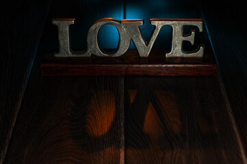 Metal Sign of the Word Love, on a Wooden Table and backlit with coloured light.