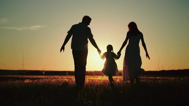 Small girl happily runs hand in hand with parents on field to release energy after day at kindergarten. Small girl loves to run across field at sunset having fun with papa and momma at sunset