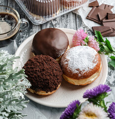 Yummy set of cake donuts with vanilla, chocolate icing, powdered sugar and chocolate chips on plate on grey background with flowers. Sweets, dessert and pastry, top view, close up