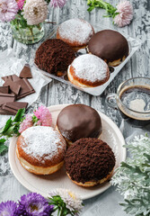 Yummy set of cake donuts with vanilla, chocolate icing, powdered sugar and chocolate chips on plate on grey background with flowers. Sweets, dessert and pastry, top view, close up