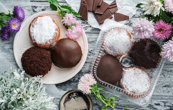 Yummy set of cake donuts with vanilla, chocolate icing, powdered sugar and chocolate chips on plate on grey background with flowers. Sweets, dessert and pastry, top view