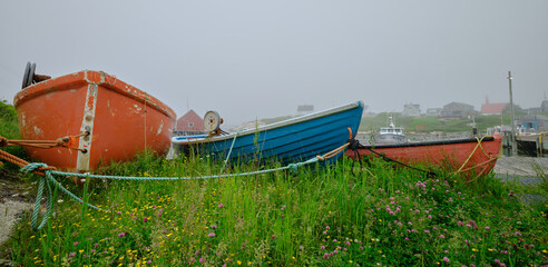 Colorful wood rowboats sit on dry land in the safety of Peggy's Cove Harbor Nova Scotia on a gray and foggy day - 736641282