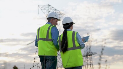 Engineer inspect power transmission lines inputting data on tablet at sunset countryside....