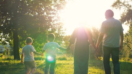 Happy children and joyful parents walk joining hands across meadow on family weekend. Small...