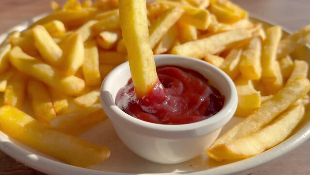 Close up on French fries dipping them in ketchup. Closeup shot of dipping French fry into ketchup with the blurry background of modern fast food cafeteria. High quality 4k footage.
