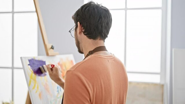 Bearded man painting on canvas in a bright art studio.