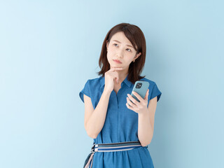 スマホを持って考える女性・ブルーバック