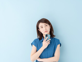 スマホを持って考える女性・ブルーバック