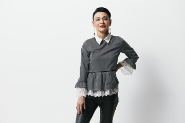 Confident young woman in trendy black leather pants and gray top posing against white wall with hands on hips