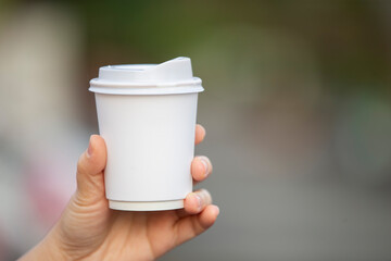 Hand holding a paper cup of coffee on blurred bokeh background