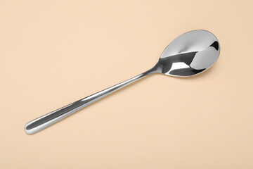 One shiny silver spoon on beige background, top view