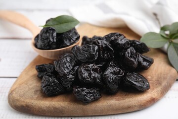 Spoon with tasty dried prunes and green leaves on light wooden table, closeup