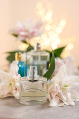 Bottles of perfume and beautiful lily flowers on table against beige background with blurred...