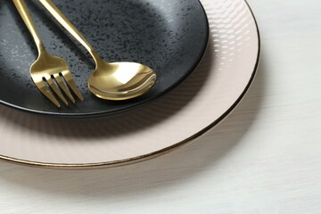 Stylish ceramic plates, fork and spoon on white wooden table, closeup