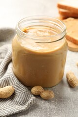 Obraz na płótnie Canvas Tasty peanut butter in glass jar and peanuts on gray table, closeup