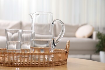 Jug and glasses with clear water on table indoors, closeup. Space for text
