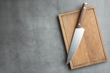 Knife and wooden board on grey textured table, top view. Space for text