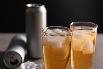 Energy drink with ice cubes in glasses and aluminium cans on table, closeup