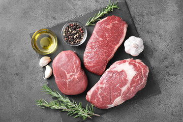 Raw beef steaks, oil and spices on grey background, top view