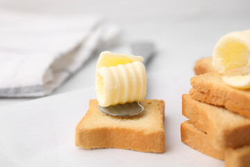Tasty butter curls, knife and pieces of dry bread on white table, closeup