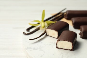 Glazed curd cheese bars, vanilla pods and flower on white table, closeup
