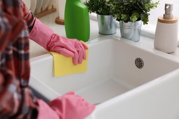 Woman cleaning kitchen sink with microfiber cloth at home, closeup