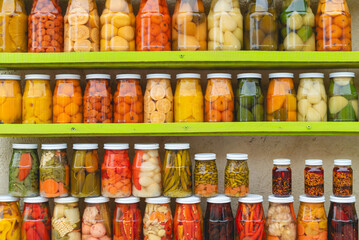 Many Jars with fruity compotes jams and pickled vegetables. Preserved fruits