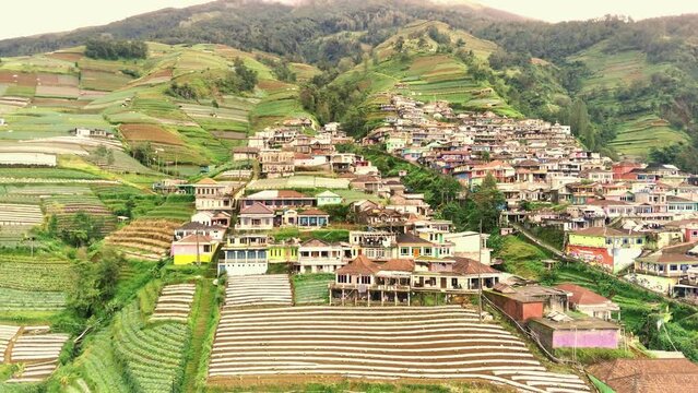 A vibrant village called Dusun Butuh or Nepal Van Java, Magelang, Indonesia with colorful houses clings to a steep hillside. Lush vegetation surrounds the houses. Aerial footage taken by drone.