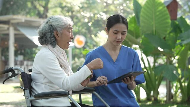 Compassionate Asian woman provides care to  elderly person in wheelchair outdoors. Engaging in physical therapy, happiness, encouraging positive environment for mature individuals with grey hair.