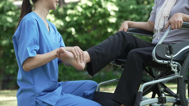 Compassionate Asian woman provides care to  elderly person in wheelchair outdoors. Engaging in physical therapy, happiness, encouraging positive environment for mature individuals with grey hair.