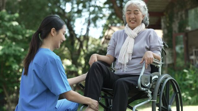 Squeeze and massage, Compassionate Asian woman provides care to  elderly person in wheelchair outdoors. Engaging in physical therapy, happiness, mature individuals with grey hair.
