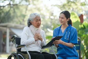 Fototapeta premium Compassionate Asian woman provides care to elderly person in wheelchair outdoors. Engaging in physical therapy, happiness, encouraging positive environment for mature individuals with grey hair.