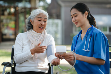 Obraz premium Compassionate Asian woman provides care to elderly person in wheelchair outdoors. Engaging in physical therapy, happiness, encouraging positive environment for mature individuals with grey hair.