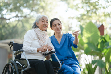 Fototapeta na wymiar Compassionate Asian woman provides care to elderly person in wheelchair outdoors. Engaging in physical therapy, happiness, encouraging positive environment for mature individuals with grey hair.
