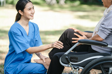 Fototapeta premium Compassionate Asian woman provides care to elderly person in wheelchair outdoors. Engaging in physical therapy, happiness, encouraging positive environment for mature individuals with grey hair.