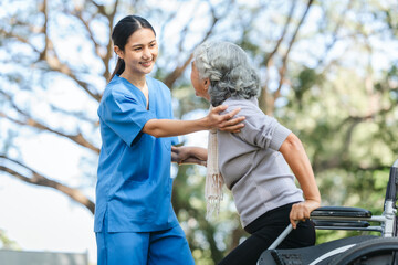 Compassionate Asian woman provides care to  elderly person in wheelchair outdoors. Engaging in physical therapy, happiness, encouraging positive environment for mature individuals with grey hair.