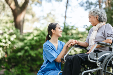 Fototapeta premium Compassionate Asian woman provides care to elderly person in wheelchair outdoors. Engaging in physical therapy, happiness, encouraging positive environment for mature individuals with grey hair.