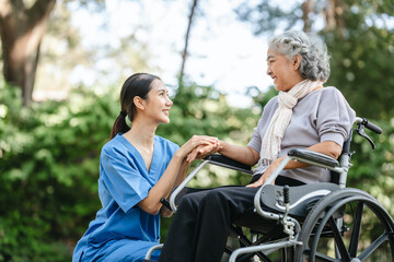 Compassionate Asian woman provides care to  elderly person in wheelchair outdoors. Engaging in physical therapy, happiness, encouraging positive environment for mature individuals with grey hair.