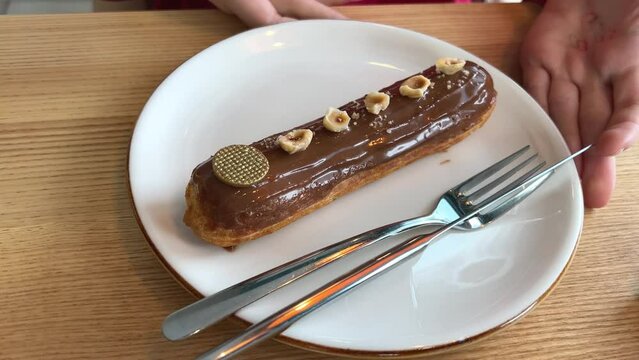 French dessert eclair, with dark chocolate glaze, chocolate glaze dripping from spoon on eclair