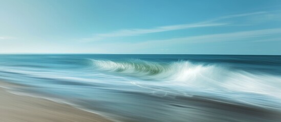 A hazy image capturing the fluid movement of waves crashing on a sandy beach under a cloudy sky with the horizon in the background