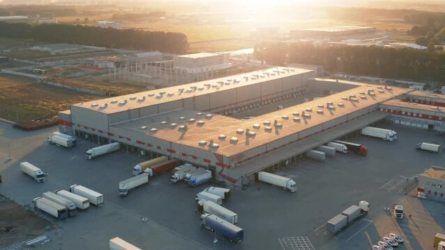 Aerial all-round view of a logistics park with a warehouses. Loading hub with many semi trucks with cargo trailers standing at ramps for load and unload goods at sunset