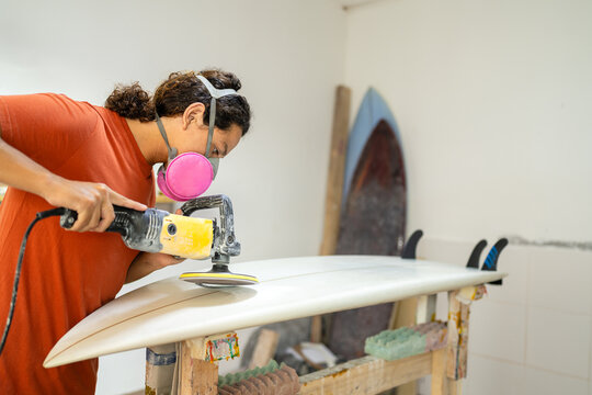 Man repairing and polishing a surfboard in a workshop