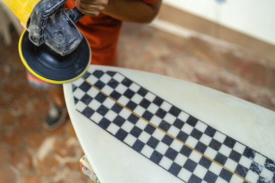 Man using an electric disc to polish a surfboard