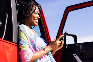 Young African American woman smiles while using her phone in a vehicle on a road trip, with copy spa